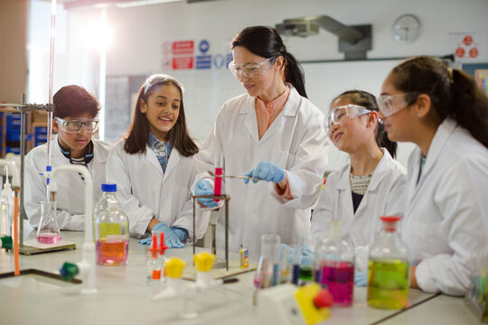 Female teacher and students conducting scientific experiment, watching liquid in test tube in laboratory classroom