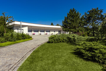 Fototapeta premium Modern garage for several cars with paved driveway surrounded by green parkland