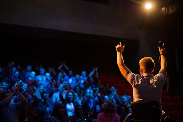 Female speaker in wheelchair on stage waving to audience
