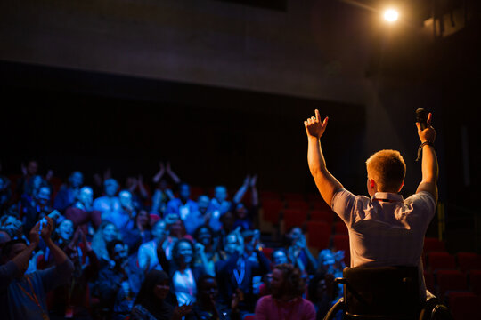 Female speaker in wheelchair on stage waving to audience