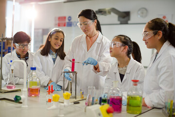 Female teacher and students conducting scientific experiment, watching liquid in test tube in laboratory classroom