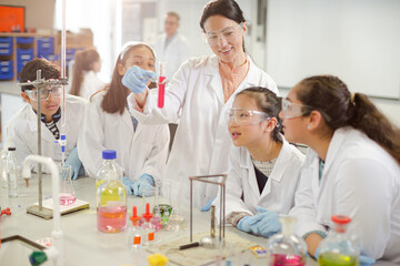 Female teacher and students conducting scientific experiment, watching liquid in test tube in laboratory classroom