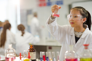 Girl student examining pink liquid, conducting scientific experiment in laboratory classroom