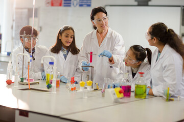 Fototapeta premium Female teacher and students conducting scientific experiment, watching liquid in test tube in laboratory classroom