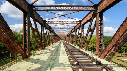 Fototapeta na wymiar Old railway line crossing a rusty bridge turned into recreational track for rail-cycle draisine with four wheels.