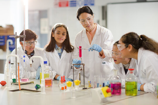 Female teacher and students conducting scientific experiment, watching liquid in test tube in laboratory classroom