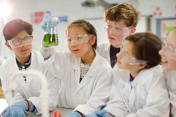 Curious students conducting scientific experiment, examining liquid in beaker in laboratory classroom