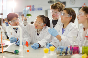 Curious students conducting scientific experiment, examining liquid in beaker in laboratory classroom