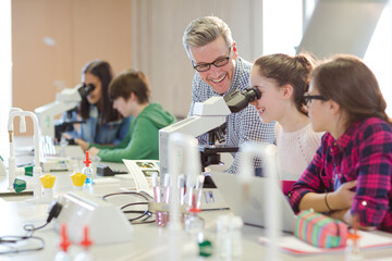 Male teacher helping girl students at microscope in laboratory classroom