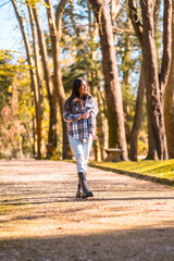 Autumn lifestyle, a young Caucasian brunette girl in a plaid wool sweater and ripped jeans in a park