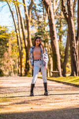 Fototapeta na wymiar Lifestyle, a young Caucasian brunette girl in a plaid wool sweater and ripped jeans in a park in autumn