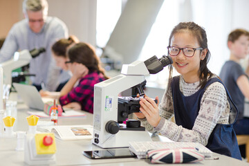 Obraz premium Portrait smiling, confident girl student using microscope, conducting scientific experiment in laboratory classroom