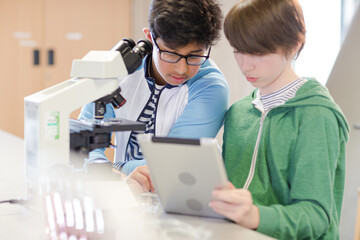Focused boy students using digital tablet at microscope in laboratory classroom