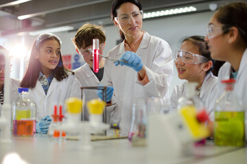 Female teacher and students conducting scientific experiment, watching liquid in test tube in...