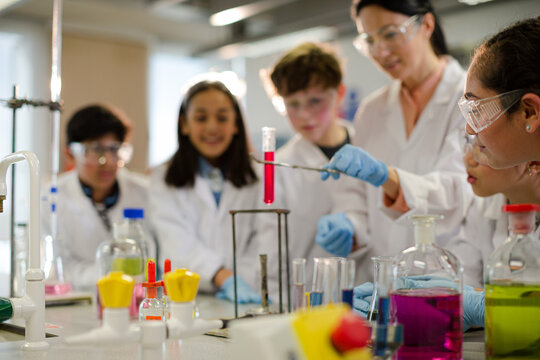 Female teacher and students conducting scientific experiment, watching liquid in test tube in laboratory classroom