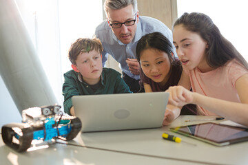 Male teacher and students using laptop in classroom