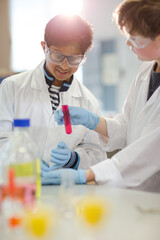 Boy students examining liquid in test tube, conducting scientific experiment in laboratory classroom