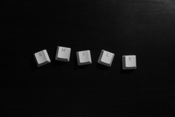 "Smile" word on white keyboard keycaps on dark wood background.