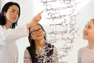 Female teacher and girl students examining hanging molecular structure