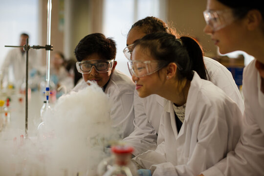 Female teacher and students watching scientific experiment chemical reaction in laboratory classroom
