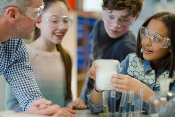 Male teacher and students watching chemical reaction, conducting scientific experiment in laboratory classroom