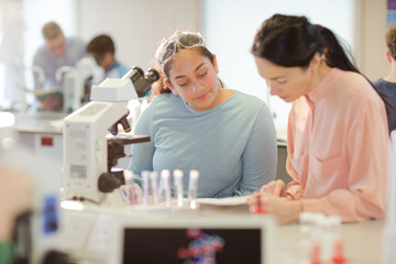Fototapeta na wymiar Female teacher and girl student conducting scientific experiment at microscope in laboratory classroom