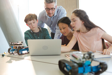 Obraz premium Male teacher and students using laptop in classroom