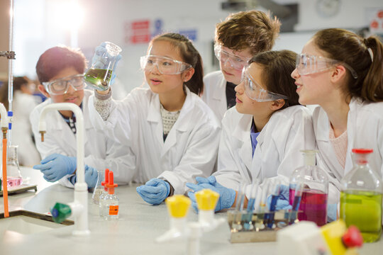 Curious students conducting scientific experiment, examining liquid in beaker in laboratory classroom