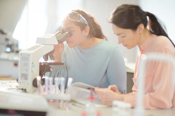 Female teacher and girl student conducting scientific experiment at microscope in laboratory...