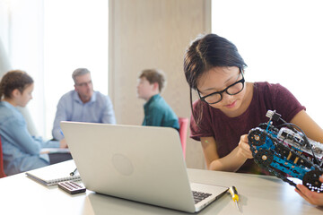 Girl student using laptop while assembling robot