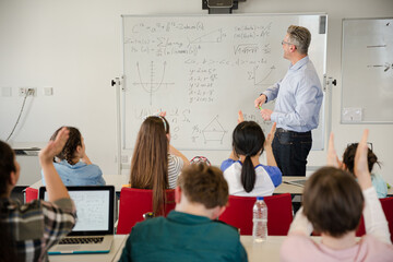 Male teacher leading lesson at whiteboard in classroom