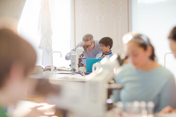 Obraz premium Male teacher and boy student conducting scientific experiment at microscope in laboratory classroom