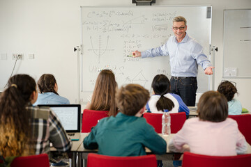 Male teacher leading lesson at whiteboard in classroom