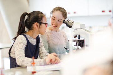 Obraz premium Girl student conducting scientific experiment at microscope in laboratory classroom