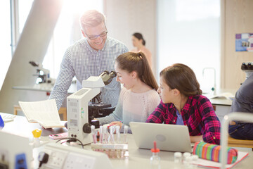 Obraz premium Male teacher helping girl students using microscope, conducting scientific experiment in laboratory classroom