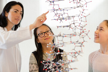 Female teacher and girl students examining hanging molecular structure