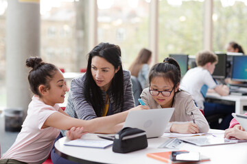 Fototapeta premium Female teacher and girl students using laptop at table