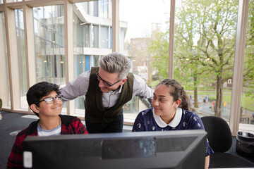 Male teacher and students using computer in library