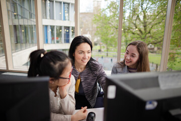 Female teacher and students using computer in library