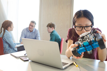 Girl student using laptop while assembling robot