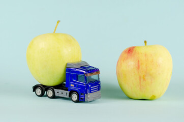 Toy truck pulling a ripe apple. Blue plastic truck and two fruits against a blue background.