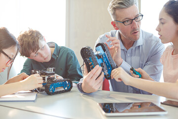 Male teacher and students playing with robot in classroom