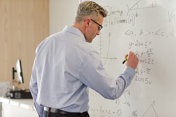 Male  teacher writing at whiteboard in classroom