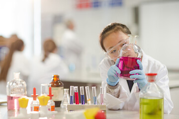 Girl student examining pink liquid, conducting scientific experiment in laboratory classroom