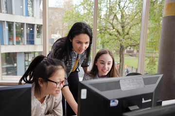 Female teacher and students using computer in library