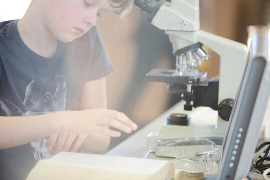 Focused boy student using microscope in classroom