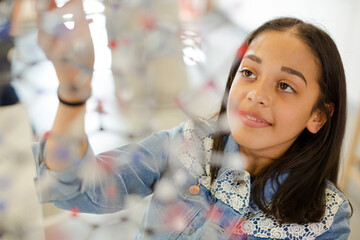 Curious girl student examining molecular structure in laboratory classroom