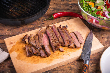 Medium well beef steak cut into pieces on a board for preparing salad with vegetables and meat