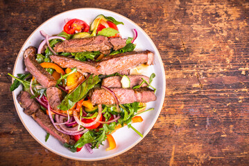 Vegetable salad with pieces of beef steak medium well in a plate, top view, copy space