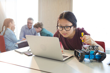 Girl student using laptop while assembling robot